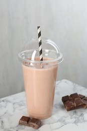 Photo of Tasty milkshake in plastic cup and chocolate pieces on white marble table