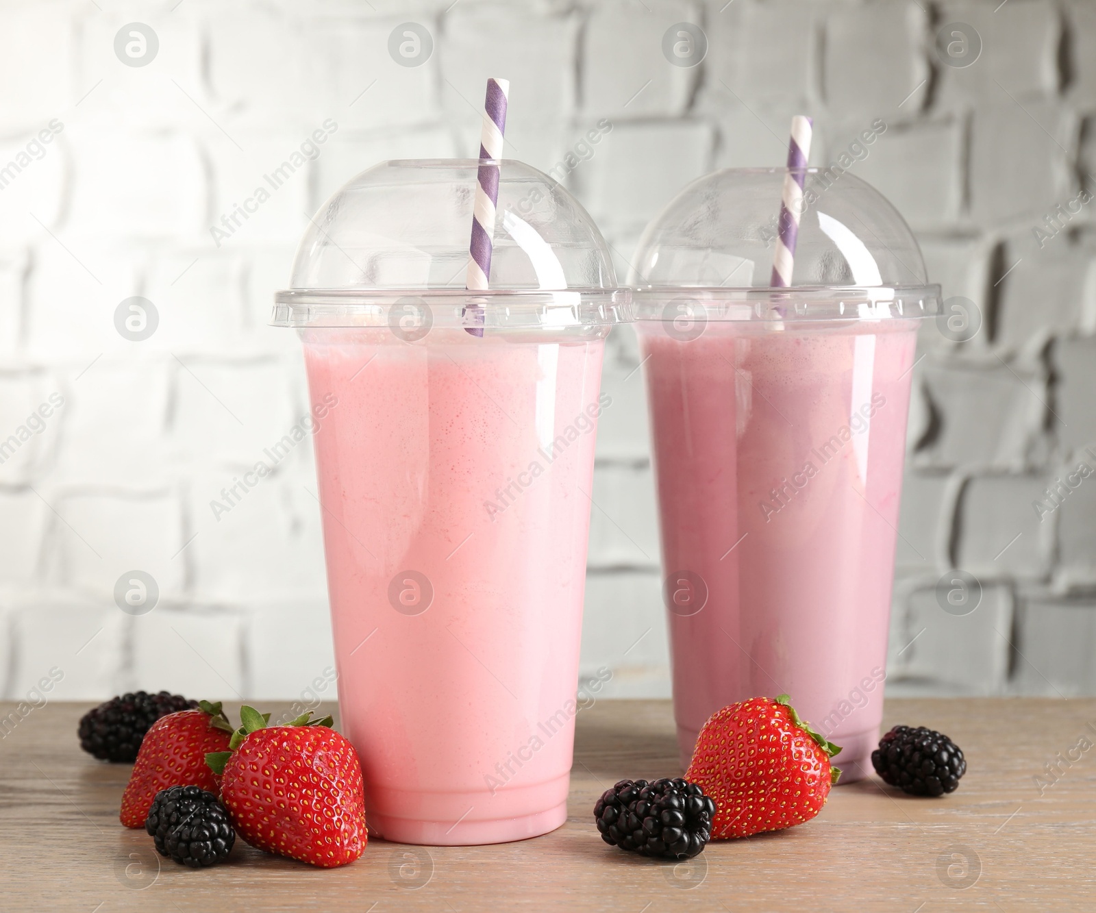 Photo of Tasty milkshakes in plastic cups and fresh berries on wooden table, closeup