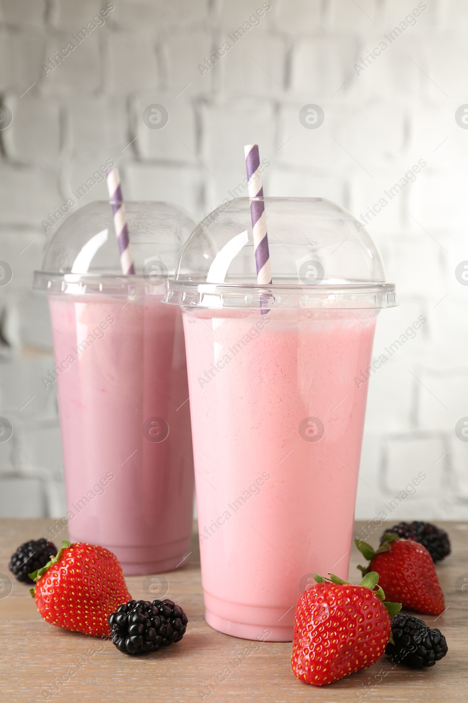 Photo of Tasty milkshakes in plastic cups and fresh berries on wooden table, closeup