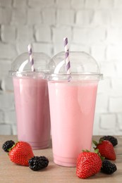 Photo of Tasty milkshakes in plastic cups and fresh berries on wooden table, closeup