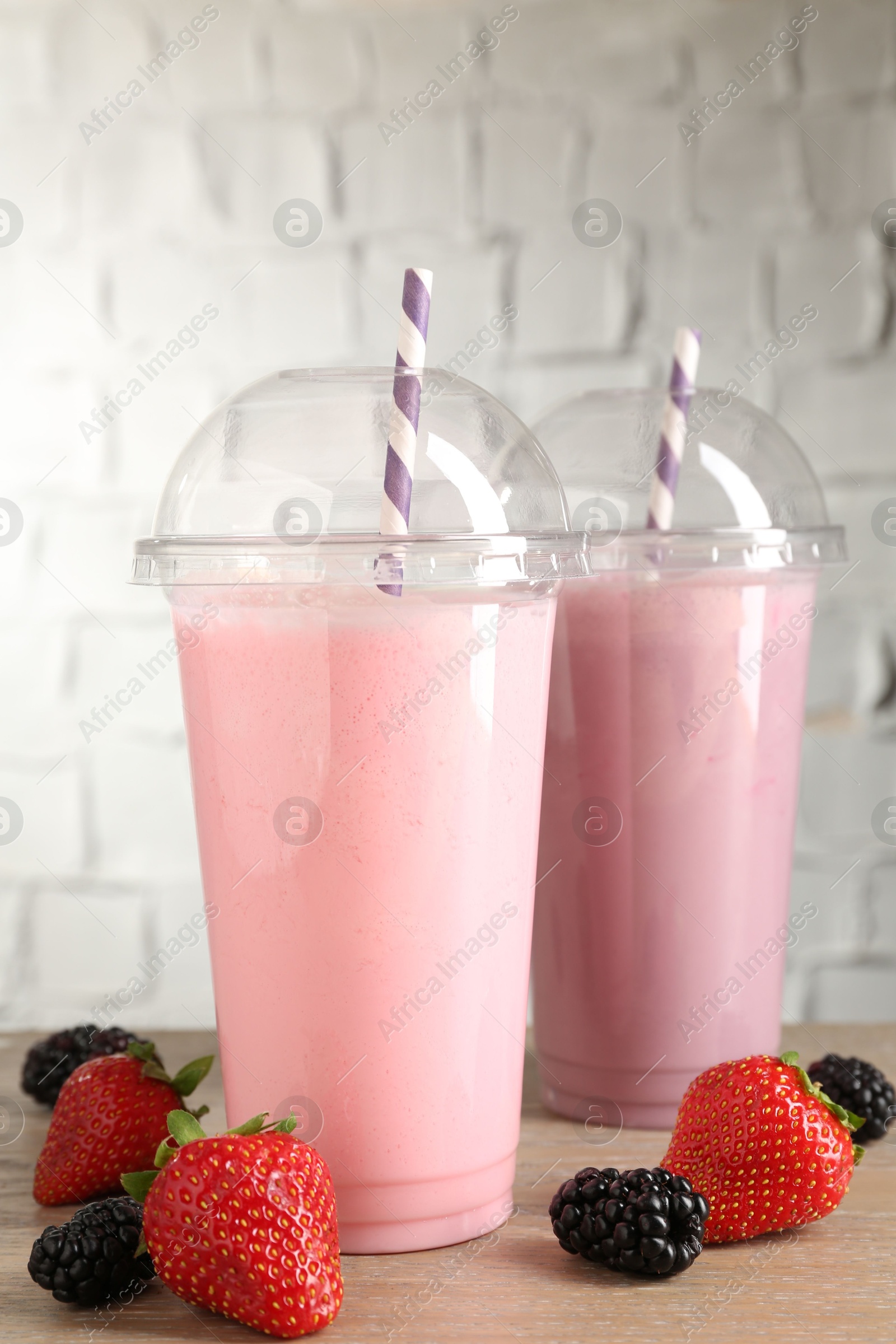 Photo of Tasty milkshakes in plastic cups and fresh berries on wooden table, closeup