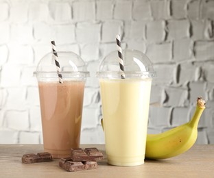Photo of Tasty milkshakes in plastic cups and ingredients on wooden table, closeup