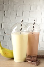 Photo of Tasty milkshakes in plastic cups and ingredients on wooden table, closeup