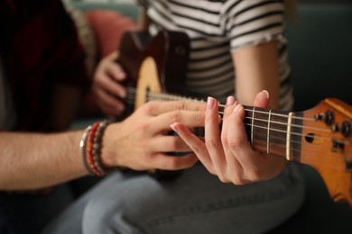 Photo of Tutor teaching woman to play guitar at home, closeup