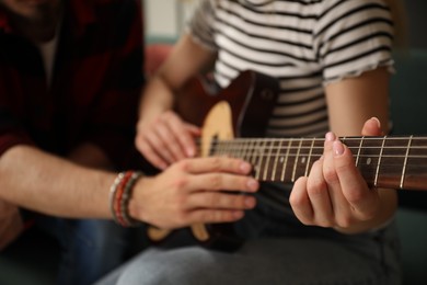 Photo of Tutor teaching woman to play guitar at home, closeup