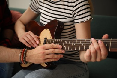 Photo of Tutor teaching woman to play guitar at home, closeup