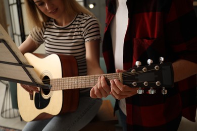 Photo of Tutor teaching woman to play guitar at home, closeup