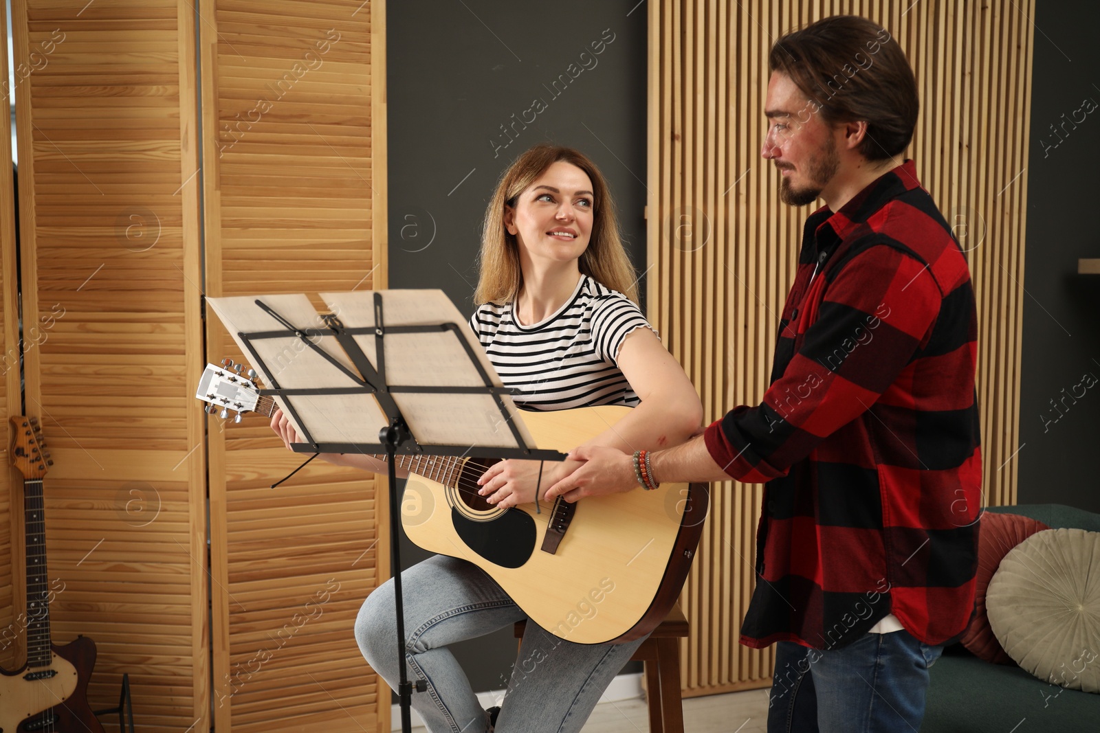 Photo of Tutor teaching woman to play guitar indoors