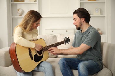 Photo of Tutor teaching woman to play guitar on sofa at home
