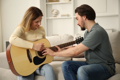 Photo of Tutor teaching woman to play guitar on sofa at home