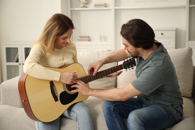 Photo of Tutor teaching woman to play guitar on sofa at home