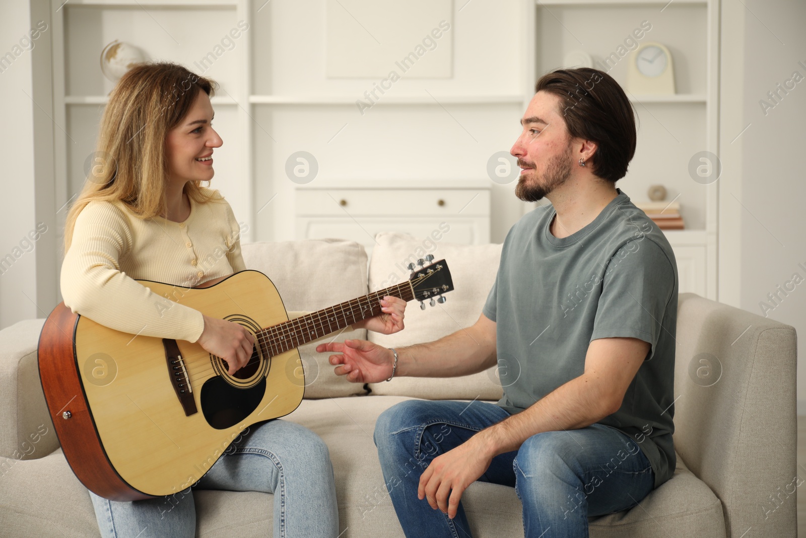 Photo of Tutor teaching woman to play guitar on sofa at home