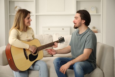 Photo of Tutor teaching woman to play guitar on sofa at home
