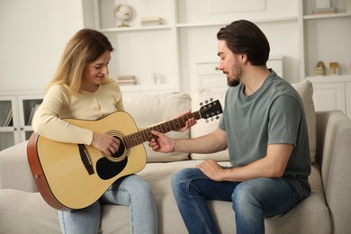 Photo of Tutor teaching woman to play guitar on sofa at home