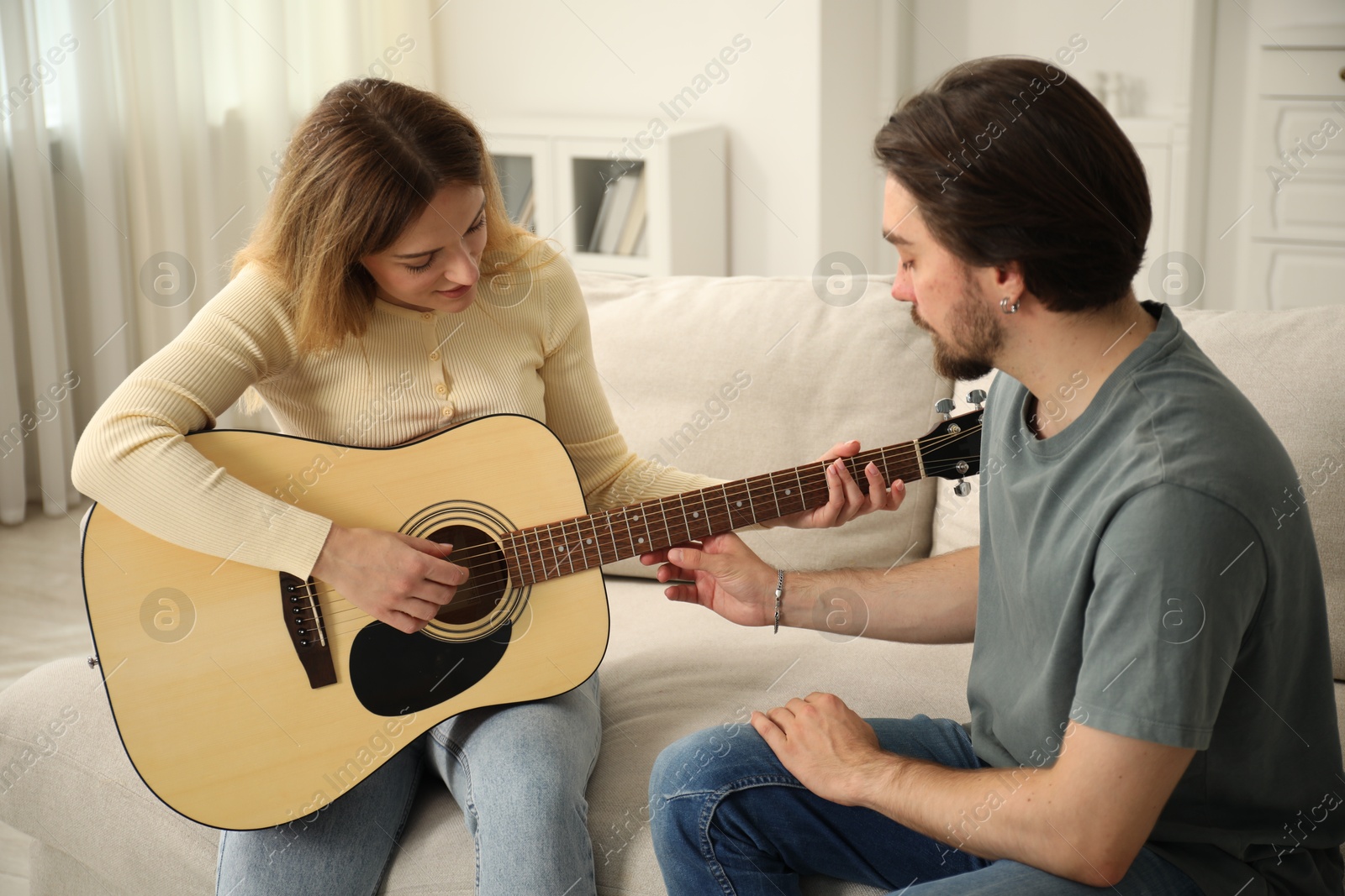 Photo of Tutor teaching woman to play guitar on sofa at home