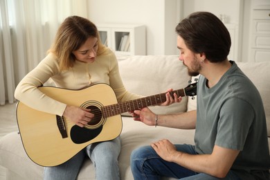 Photo of Tutor teaching woman to play guitar on sofa at home