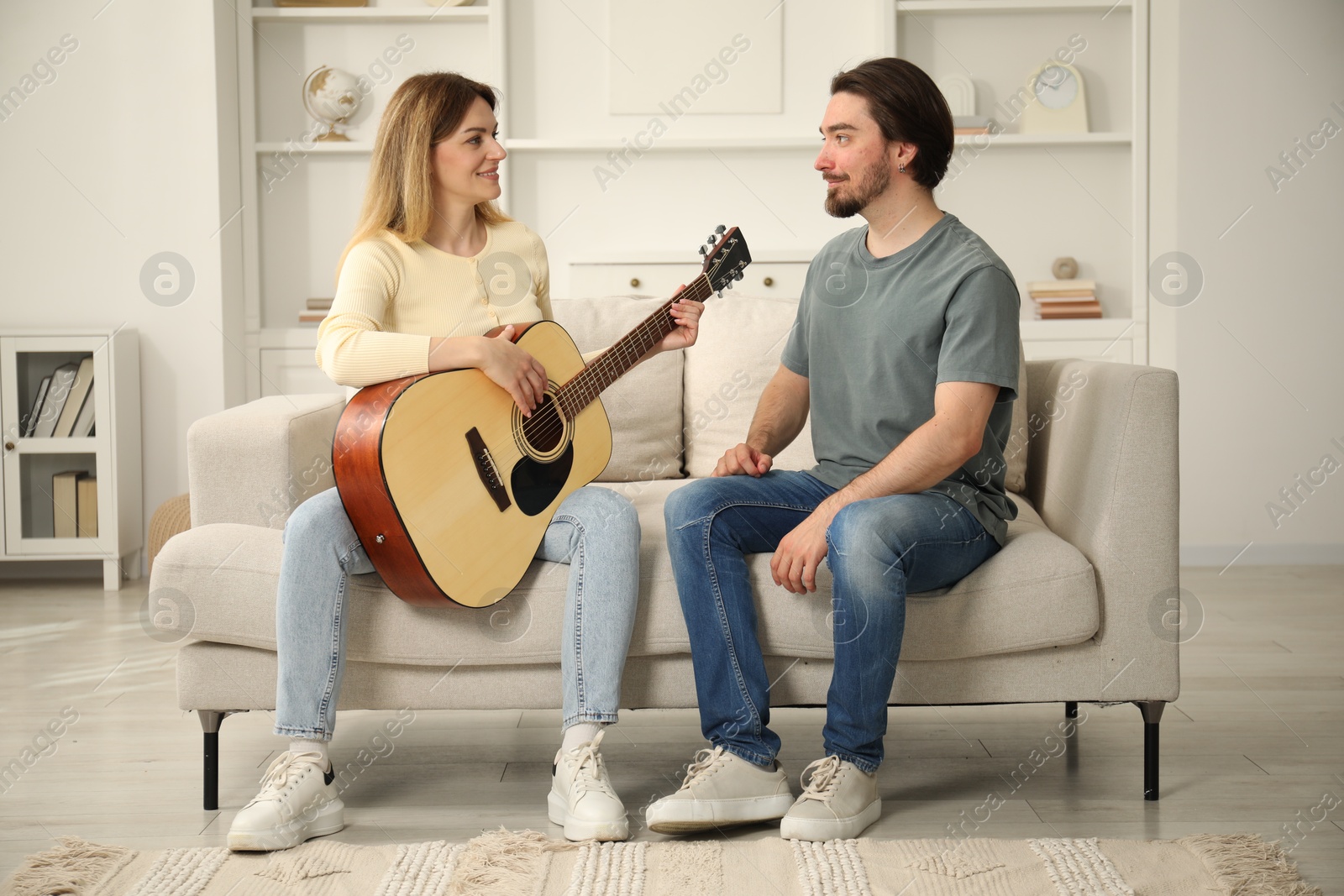 Photo of Tutor teaching woman to play guitar on sofa at home