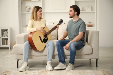 Photo of Tutor teaching woman to play guitar on sofa at home