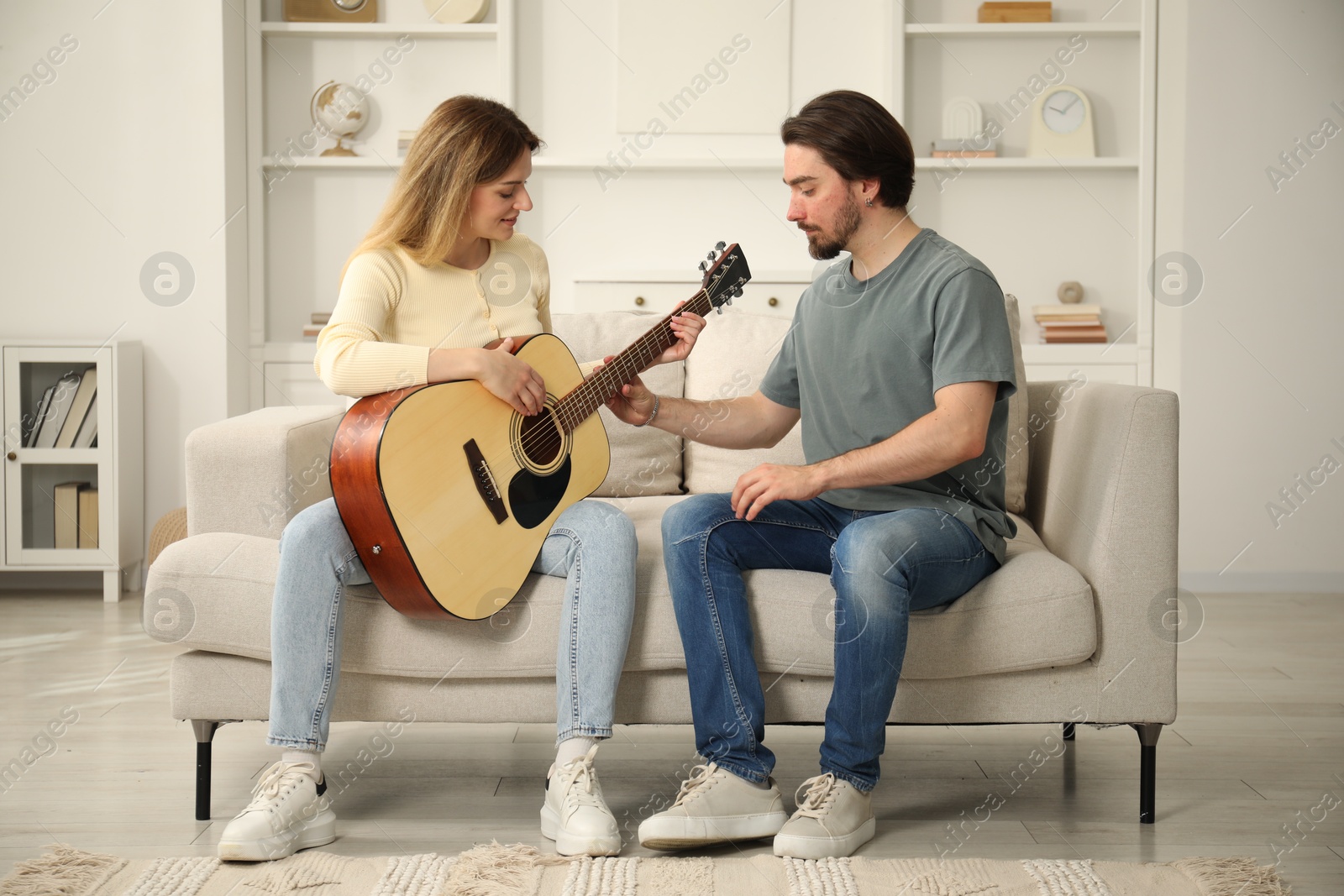Photo of Tutor teaching woman to play guitar on sofa at home