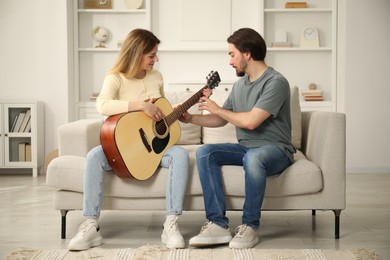Photo of Tutor teaching woman to play guitar on sofa at home