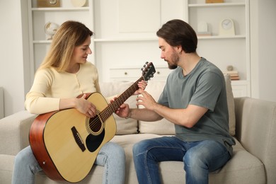 Photo of Tutor teaching woman to play guitar on sofa at home
