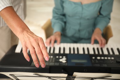 Photo of Tutor teaching woman to play piano indoors, closeup