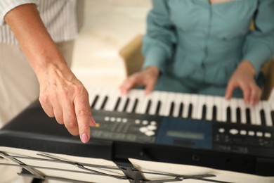 Photo of Tutor teaching woman to play piano indoors, closeup