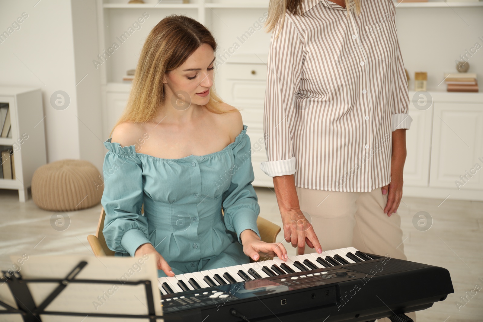 Photo of Tutor teaching woman to play piano indoors, closeup