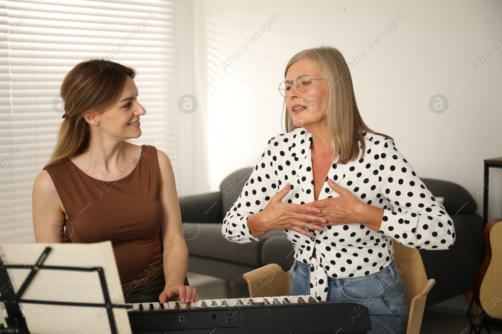 Photo of Tutor teaching woman to play piano indoors