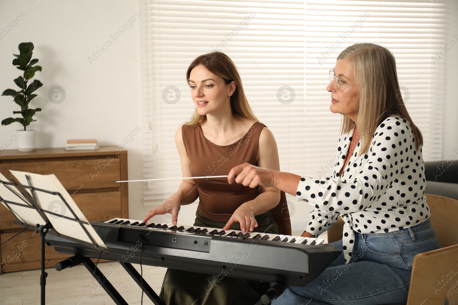 Photo of Tutor teaching woman to play piano indoors
