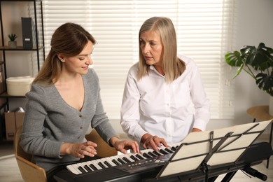 Photo of Tutor teaching woman to play piano indoors
