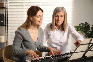 Photo of Tutor teaching woman to play piano indoors