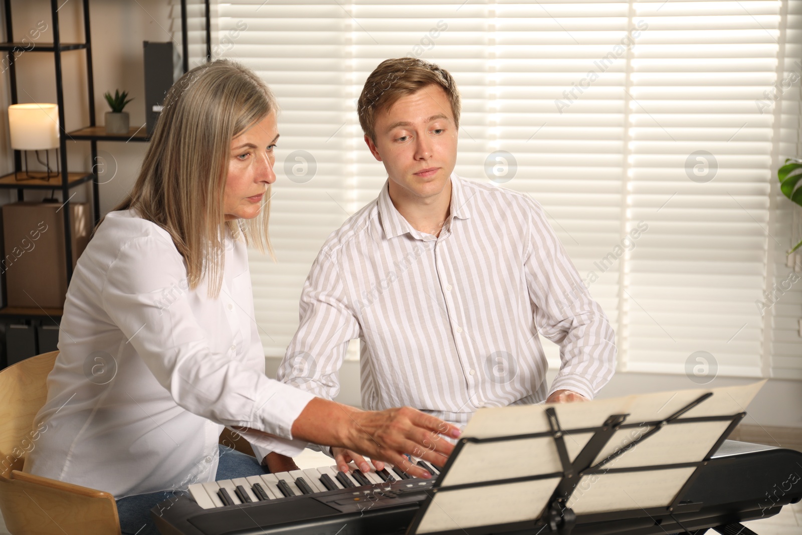 Photo of Tutor teaching man to play piano indoors