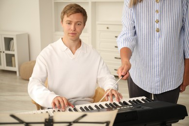 Photo of Tutor teaching man to play piano indoors, closeup