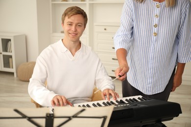 Photo of Tutor teaching man to play piano indoors, closeup