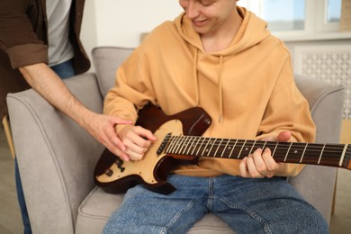 Photo of Tutor teaching man to play guitar at home, closeup