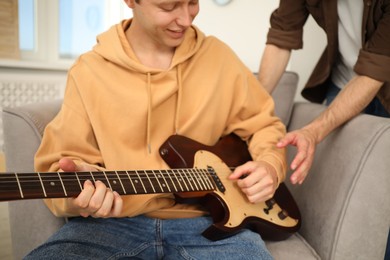 Photo of Tutor teaching man to play guitar at home, closeup
