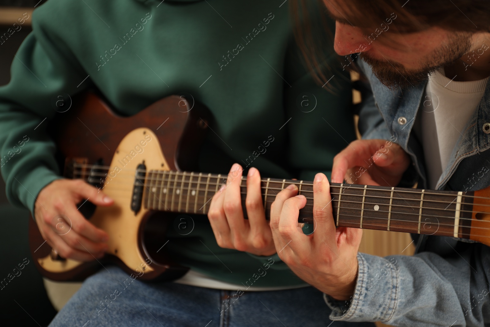 Photo of Tutor teaching man to play guitar at home, closeup