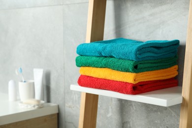 Photo of Fresh colorful terry towels on shelf in bathroom, closeup. Space for text