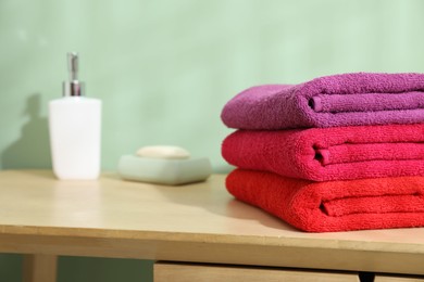 Photo of Fresh colorful terry towels and hygiene products on wooden table in bathroom, closeup