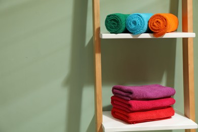 Photo of Fresh colorful terry towels on shelving unit in bathroom. Space for text