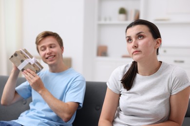 Photo of Woman feeling jealous of man receiving gift at home, selective focus