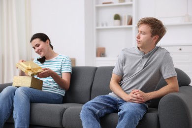 Photo of Man feeling jealous of woman receiving gift at home, selective focus