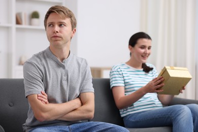 Photo of Man feeling jealous of woman receiving gift at home, selective focus