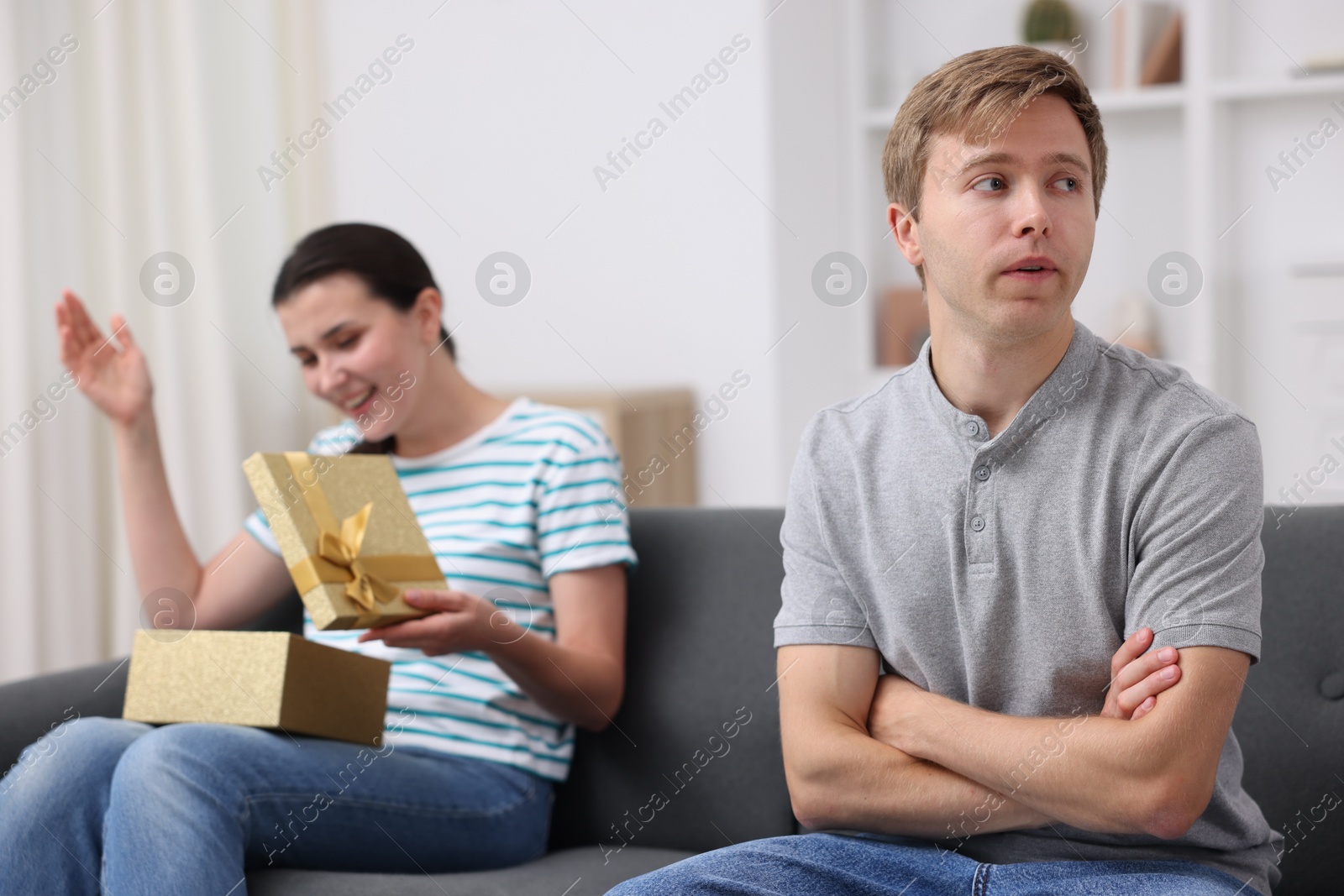 Photo of Man feeling jealous of woman receiving gift at home, selective focus