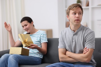 Photo of Man feeling jealous of woman receiving gift at home, selective focus