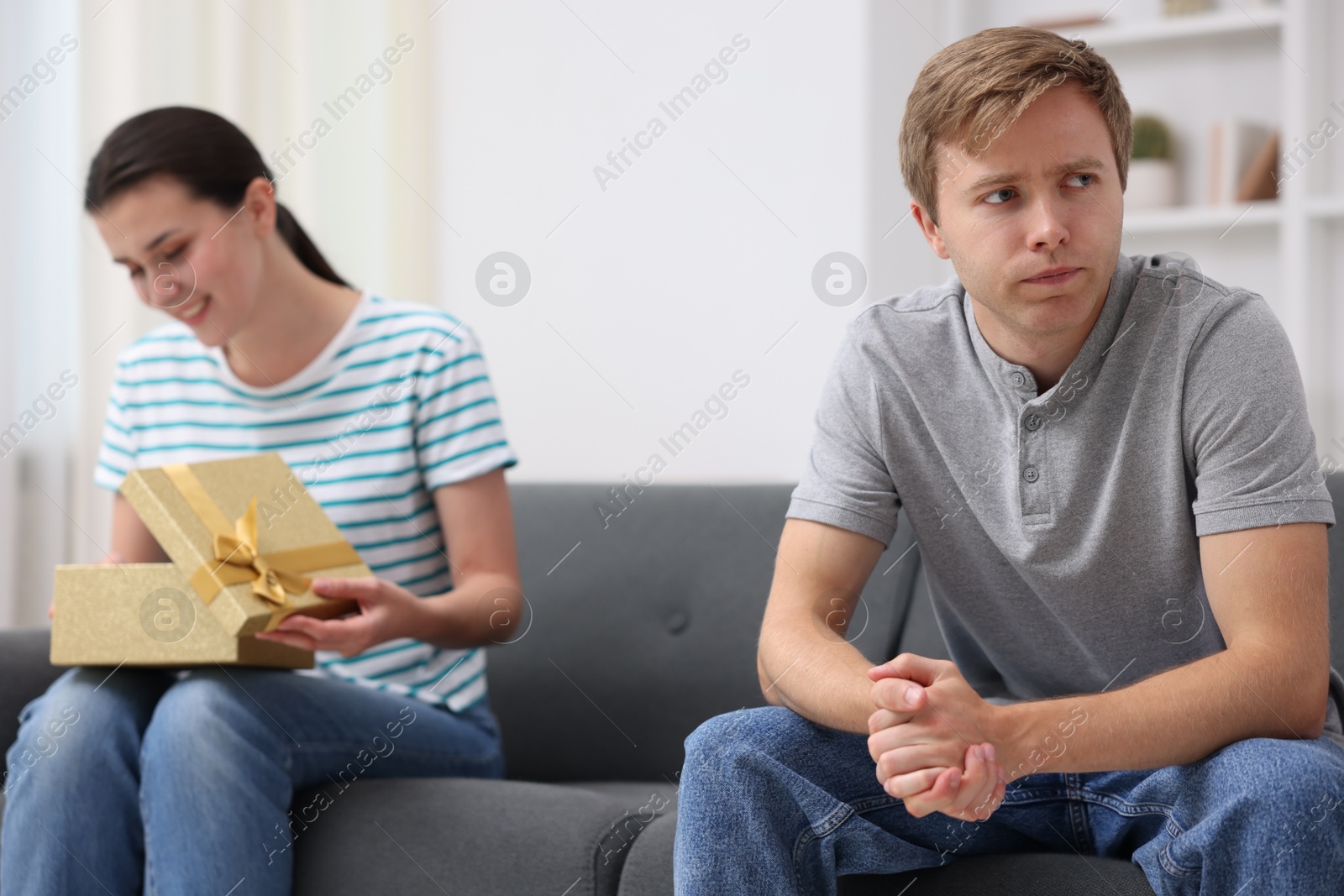Photo of Man feeling jealous of woman receiving gift at home, selective focus
