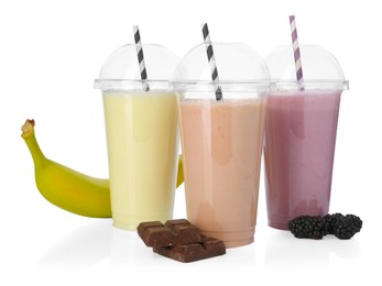 Photo of Milkshakes of different flavors in plastic cups and ingredients isolated on white