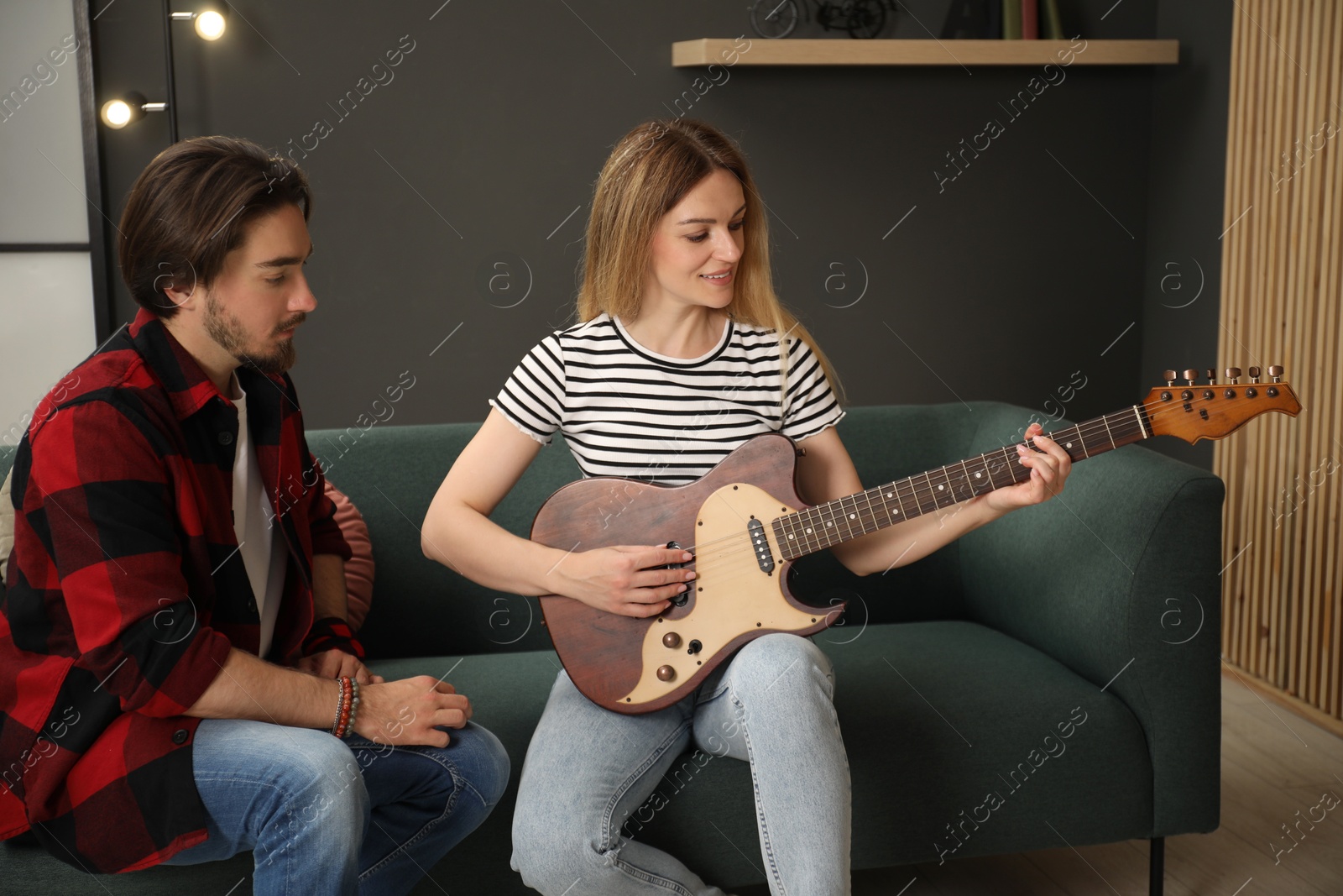 Photo of Tutor teaching woman to play guitar on sofa at home