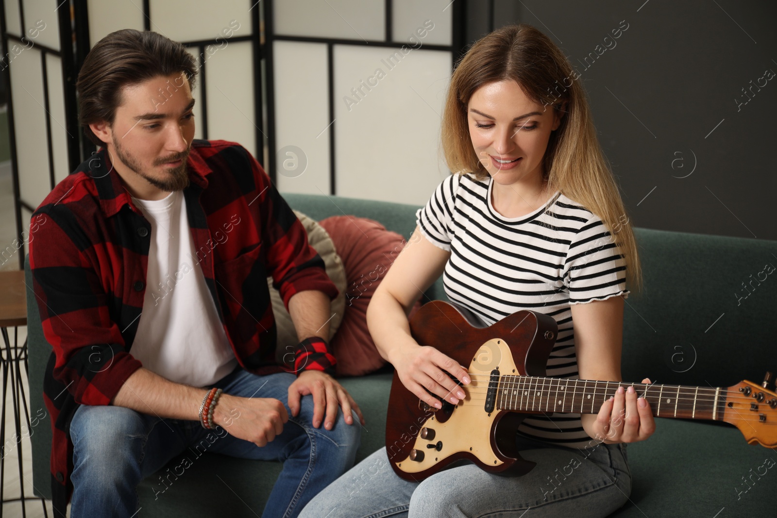 Photo of Tutor teaching woman to play guitar on sofa at home